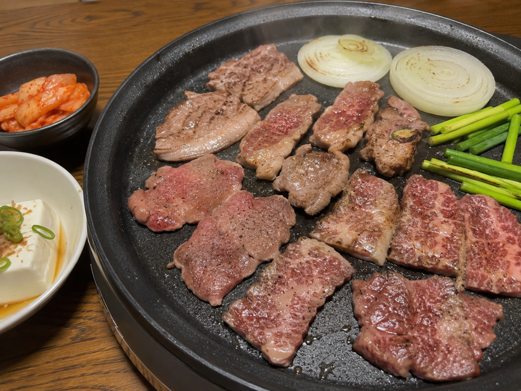 ホットプレートでラム肩ロース・牛タン・牛カイノミと玉ねぎ、ニンニクの茎を焼いている家焼肉
