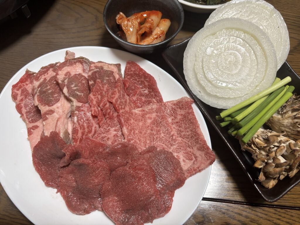 ラム肩ロース・牛タン・牛カイノミと玉ねぎ、ニンニクの茎、キムチを並べたホットプレート焼肉の家飲み準備