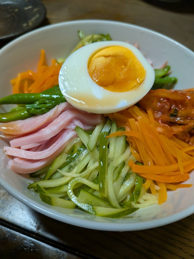 冷やし中華にのせたきゅうり、にんじん、アスパラ、ハム、ゆで卵、キムチの具材アップ