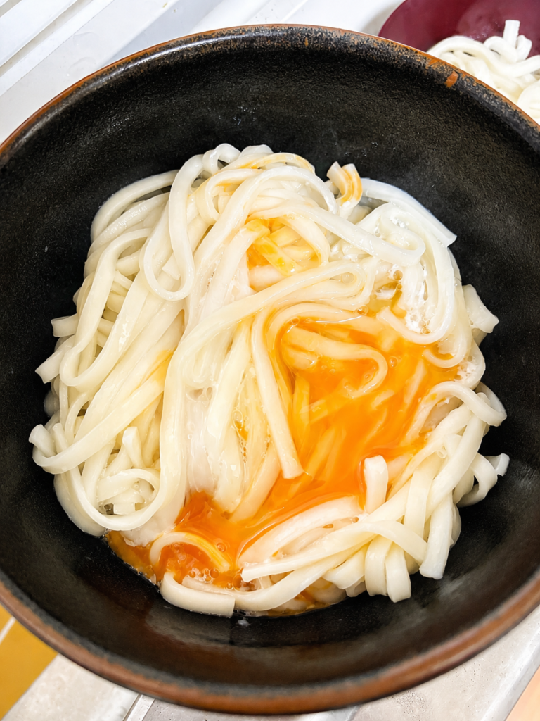 茹でたての讃岐うどんを生卵に絡める様子