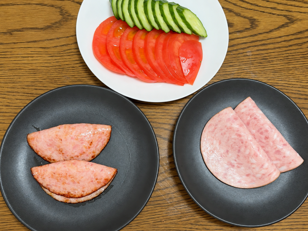 そのままと焼いたシャウスライスを黒い皿に盛り付け、トマトときゅうりを添えた食べ比べ