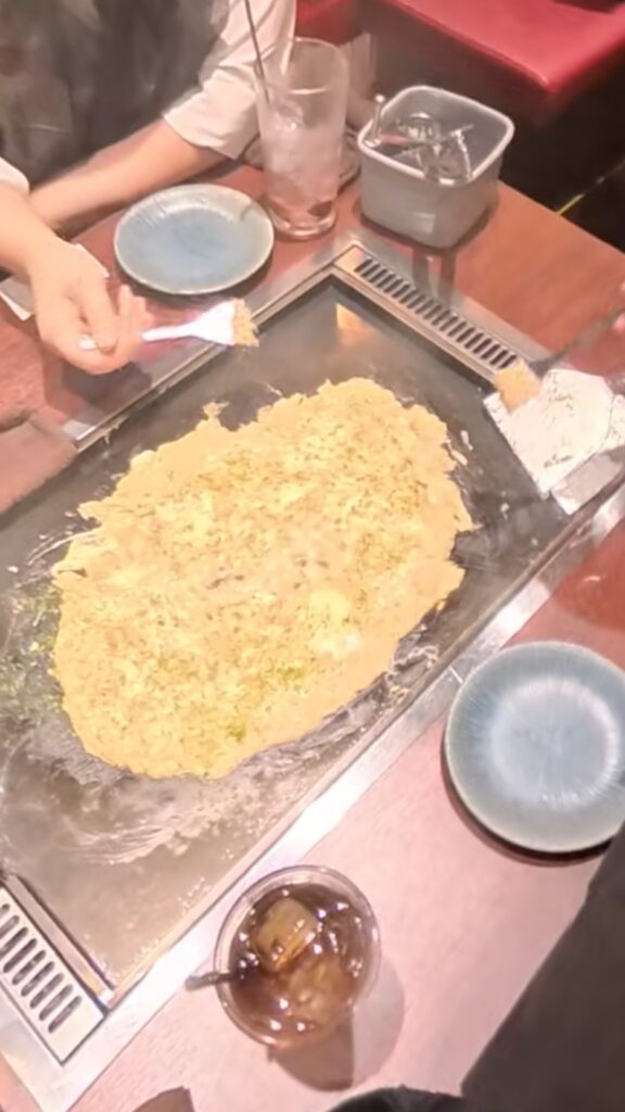 焼き上がったもんじゃ焼きを小さなヘラで取り分けて食べている様子。