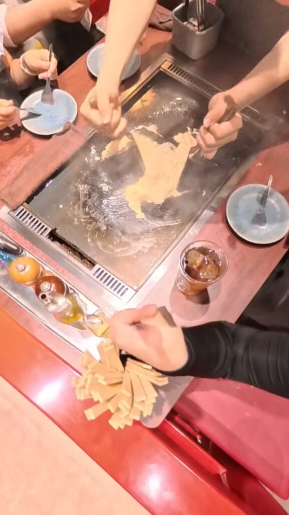 もんじゃ焼きをヘラで広げながら焼き上げている様子。