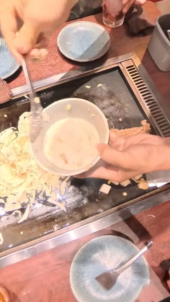五目もんじゃの具材を鉄板の上で店員さんが手際よく混ぜている様子。