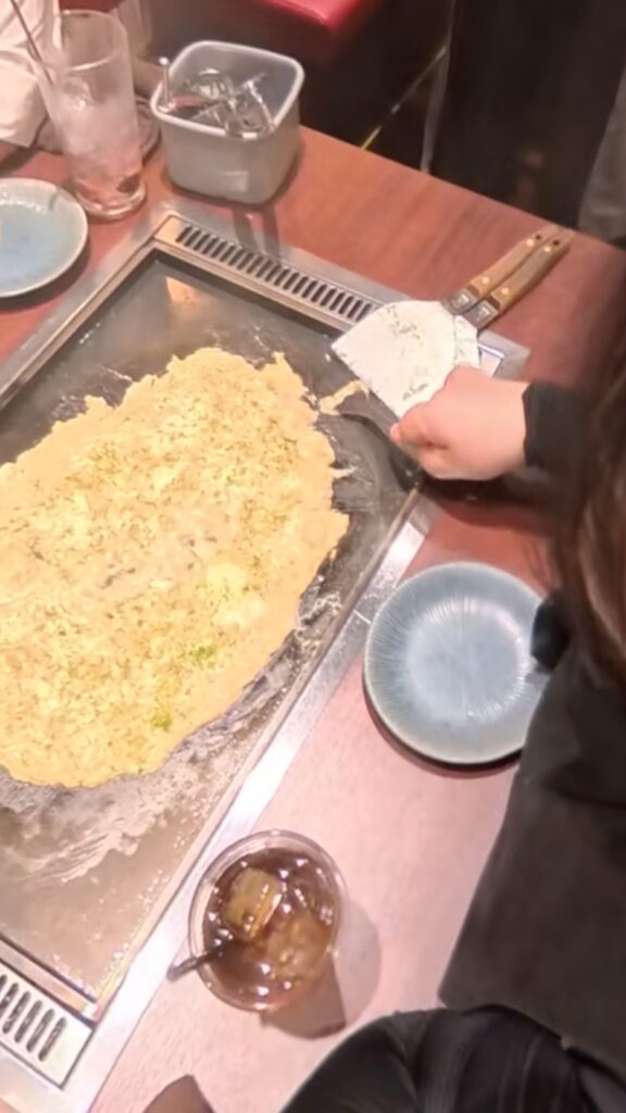 鉄板の上で明太子もちもんじゃにチーズをトッピングした調理の様子。